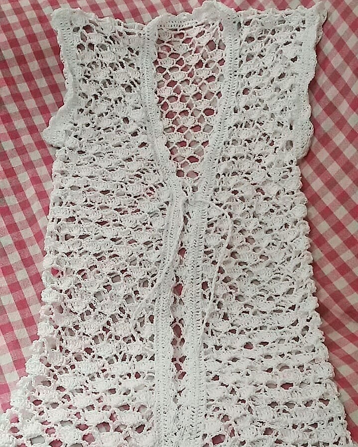 White lace beach cover-up displayed on checkered background, ideal for layering as a stylish cardigan, handmade with 100% cotton for a breezy and chic beach look.