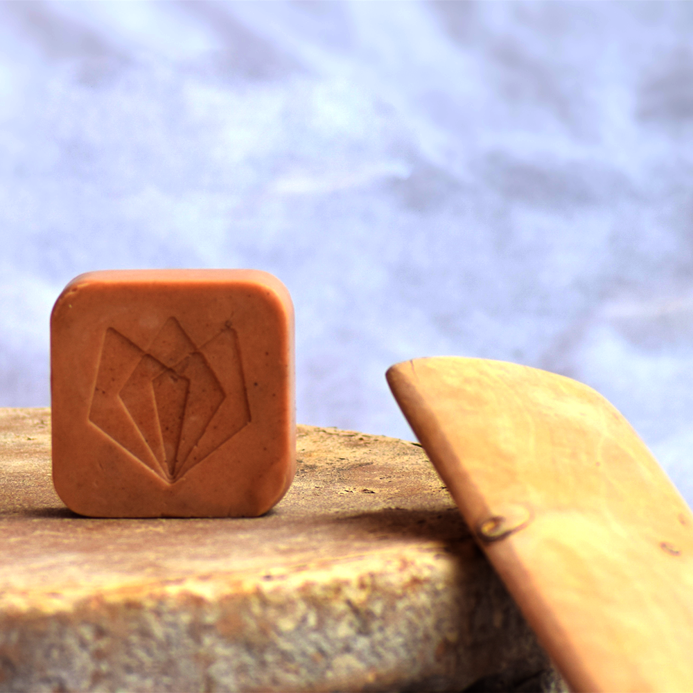 
                  
                    Mysorewood Bathing Bar (100g) with rejuvenating sandalwood and essential oils placed on a natural stone surface.
                  
                